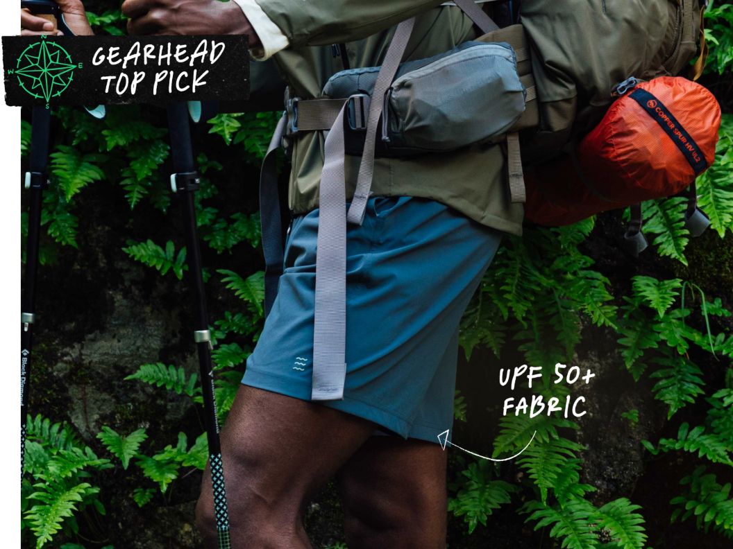 A man carries a loaded backpack and wears blue shorts. Text overlay reads: Gearhead top pick, UPF 50+ fabric.